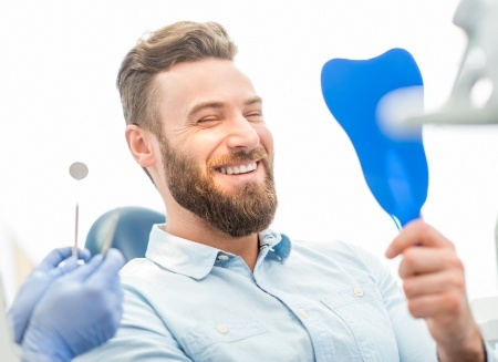 Bearded man in dental chair admiring his smile in mirror