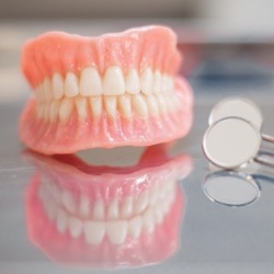 Full dentures on table next to two dental mirrors