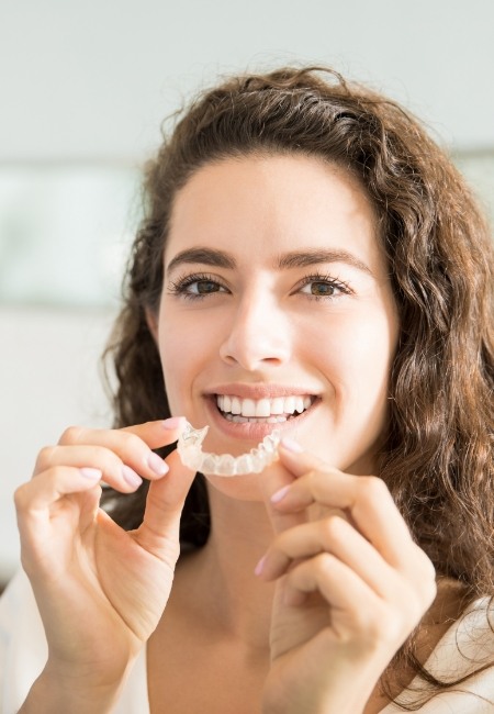 Smiling woman holding Invisalign in Sachse 