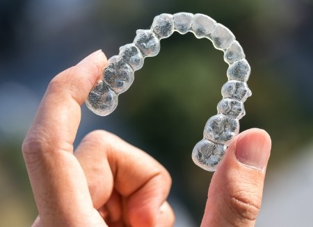 Hand holding an Invisalign aligner outdoors