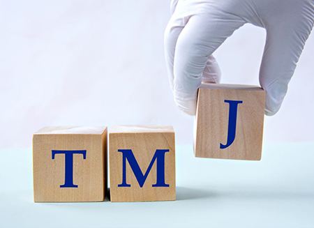 Gloved hand arranging blocks to say TMJ