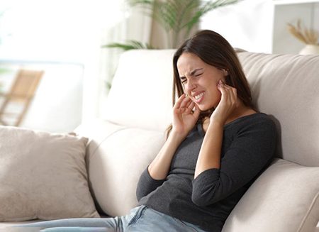 Woman grimacing due to pain of TMJ disorder