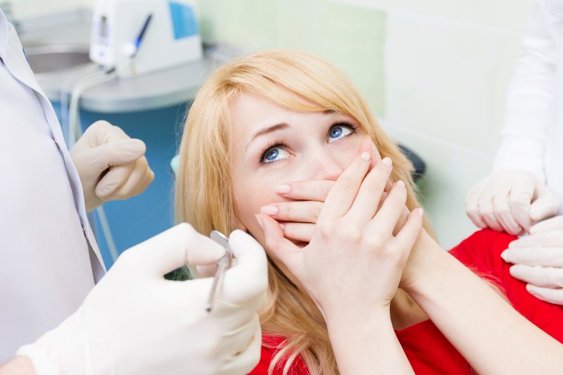 A woman covering her mouth at the dentist due to dental anxiety
