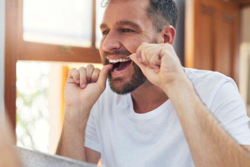 Man in white t-shirt flossing teeth