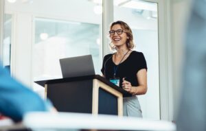 Woman smiling and standing behind podium giving presentation.